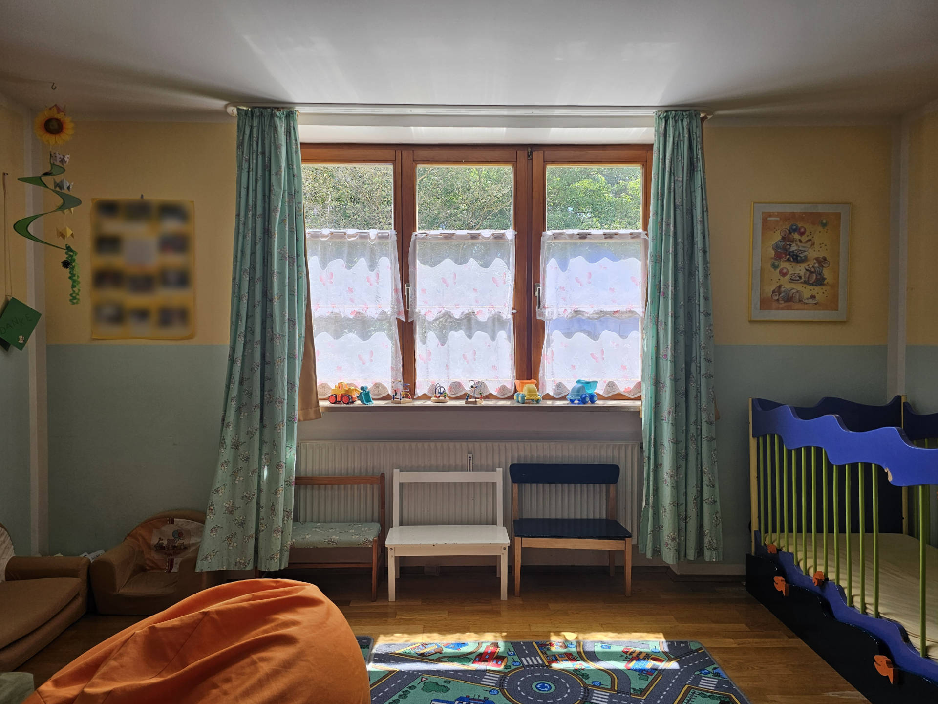 Helles, sonniges Spielzimmer für die Kinder mit einem großen Straßenteppich, einem gemütlichen Sitzsack und kleinen Bänken.