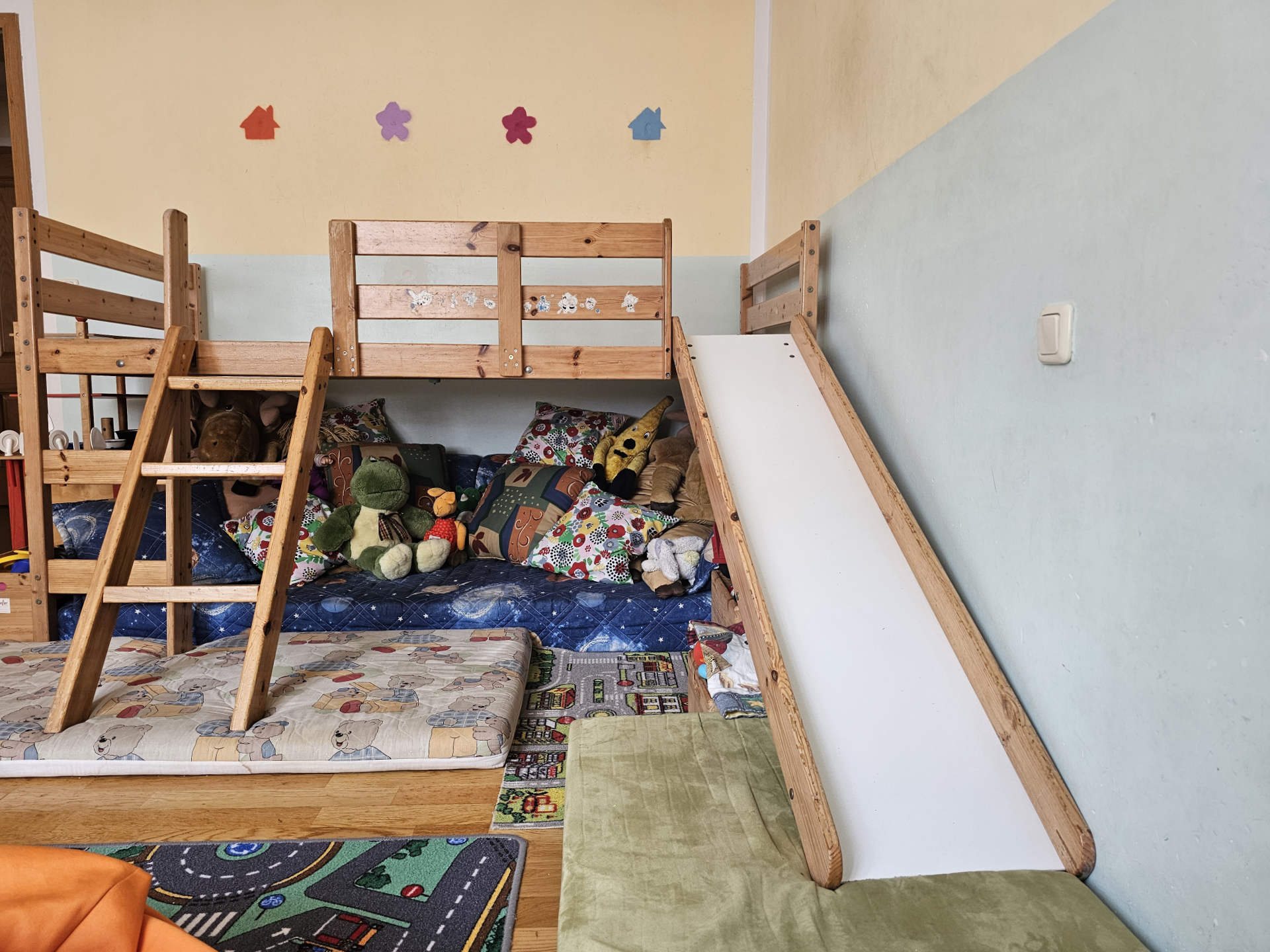 Liebevoll eingerichtetes Spielzimmer unserer Kindertagespflege mit einem Holzbett, einer kleinen Indoor-Rutsche und weichen Spielmatten.