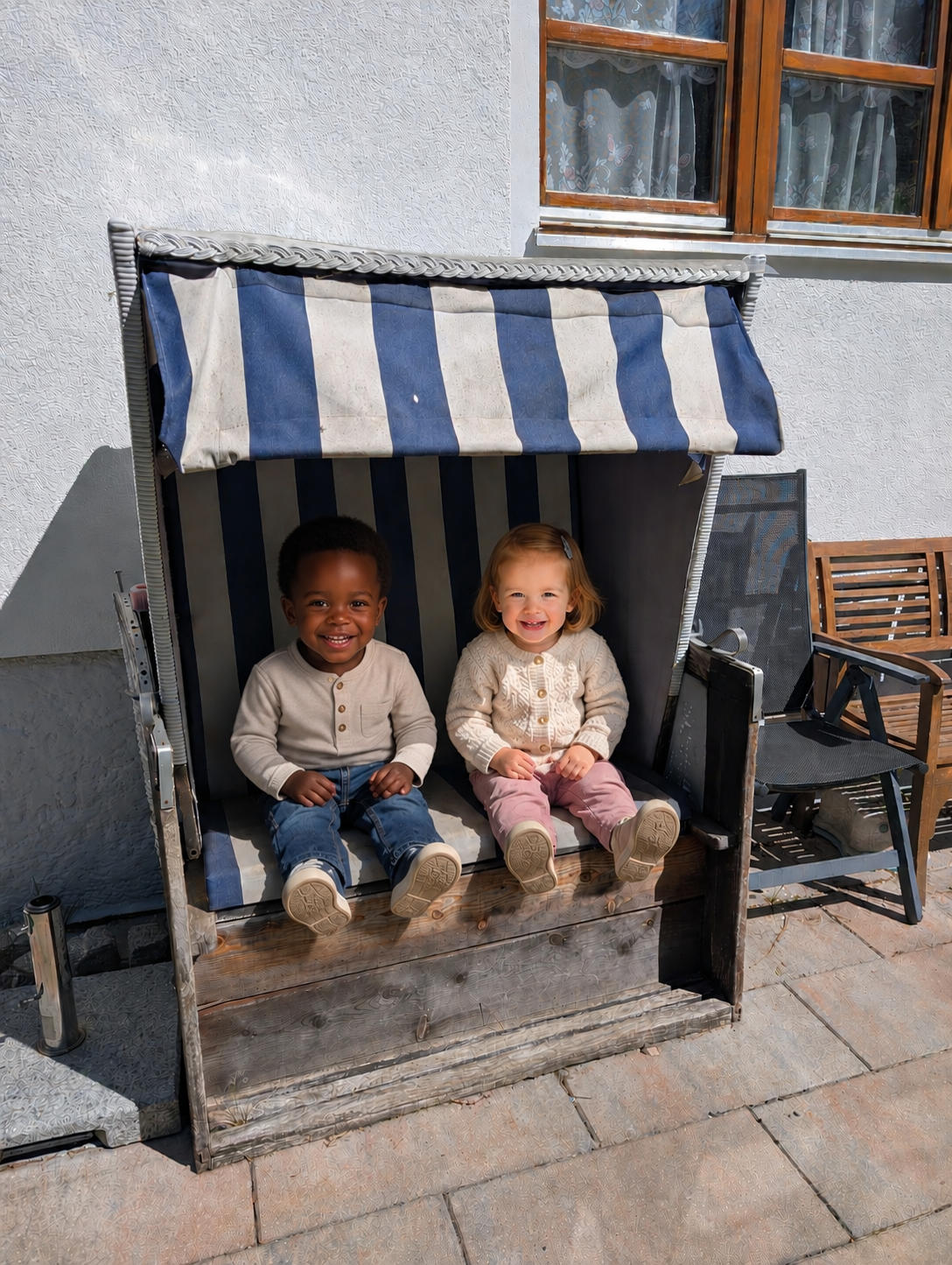 Zwei fröhliche Kinder sitzen gemeinsam lachend in unserem gemütlichen, blau-weiß gestreiften Strandkorb.